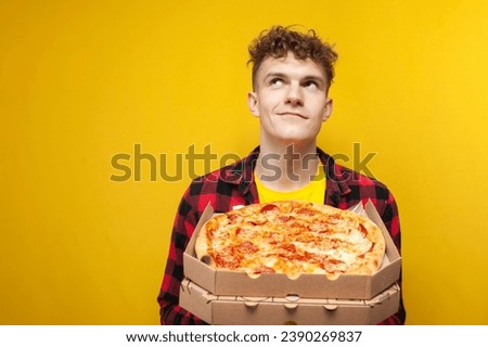 young curly cute guy with pizza looking away and dreaming, pensive man holding pizza on yellow background