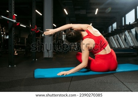 athletic woman in red sportswear sitting on yoga matte in black gym and warming up, girl doing yoga and stretching, attractive woman in fitness club doing flexibility exercise Royalty-Free Stock Photo #2390270385