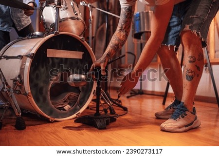 Close up image of tattooed hands setting up a recording mic in front of the bass drum in a music studio. Music recording equipment, silent isolation room. Cropped picture of a technician setting a mic