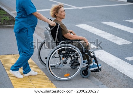 Profile of a nurse helping an elderly woman in a wheelchair cross the road. 