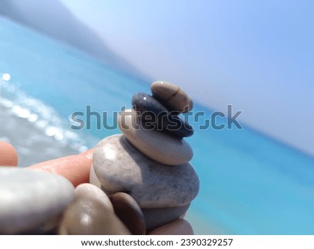 Stones stacked on top of each other in my palm.  Sunlight shines on them.  A turquoise blue, calm, wonderful sea in the background.  A clear blue cloudless sky.  2023 Turkey
