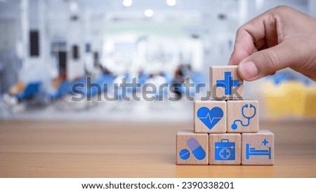 Health insurance and healthcare concept, human hand holds wooden block with icons about health insurance and healthcare access, retirement planning on wooden background.