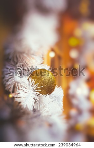 Glittering golden christmas bauble decorations on whte christmas tree branch with blurred warm lighs on the background, vintage film colored image