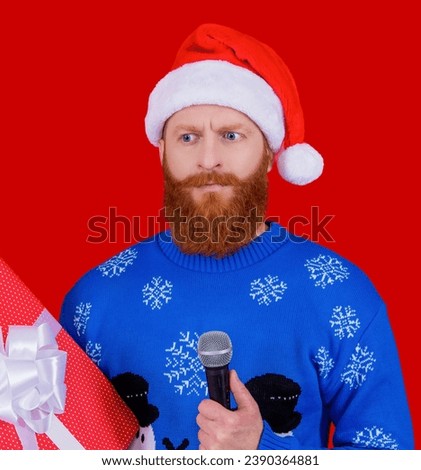 Santa Claus bearded man in Xmas hat and Christmas winter sweater hold present and microphone for new year holiday celebration isolated on red