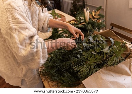Top view composition of female hands, which tie natural branches of spruce, pine, eucalyptus to botanical base with twine. Girl makes an Advent Christmas wreath. Close-up of handmade work process