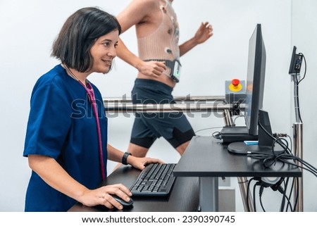 Patient walking along a treadmill performing a cardiovascular stress test while a cardiologist female doctor monitoring it Royalty-Free Stock Photo #2390390745