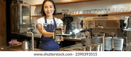 Smiling asian barista, coffee shop staff gives you credit card machine, processing payment with POS terminal, working in cafe. Royalty-Free Stock Photo #2390393515