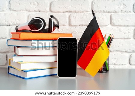 Stack of books and flag of Germany on desk. German language learning concept