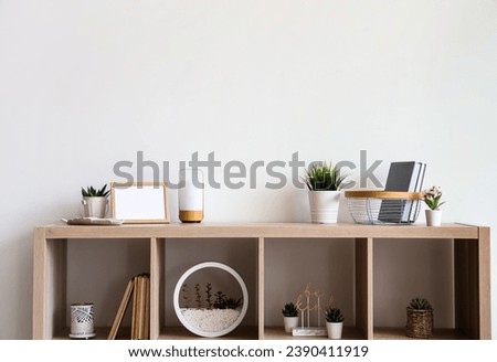 Wooden shelving unit with different houseplants and books near white wall