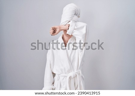 Blonde caucasian woman wearing bathrobe covering eyes with arm, looking serious and sad. sightless, hiding and rejection concept  Royalty-Free Stock Photo #2390413915