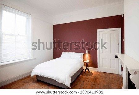 Interior of modern bedroom with double bed and white linen, color ful wall with patterns. Accent wall with maroon and blue diagonal wall paint. 