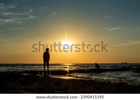 Sunset at sea with people in silhouette on a wooden post breakwater
