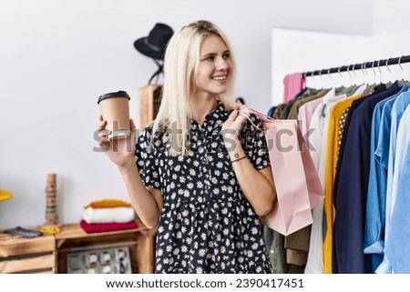 Young blonde woman smiling confident holding shopping bags and coffee at clothing store