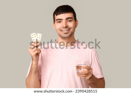 Young man with blisters of vitamin A pills and water on light background