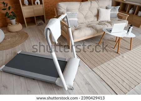 Modern treadmill with towel in living room interior