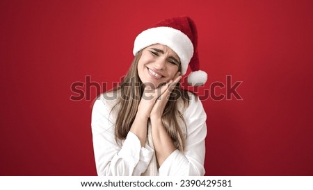 Young beautiful hispanic woman smiling confident wearing christmas hat with hands on face over isolated red background
