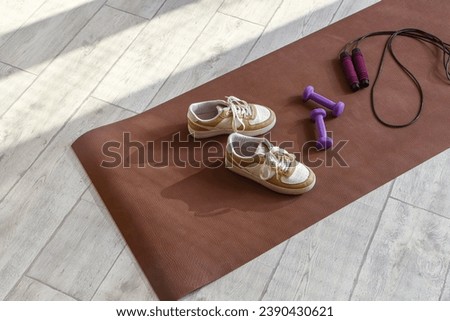 Fitness mat with sneakers, dumbbells and skipping rope on floor Royalty-Free Stock Photo #2390430621