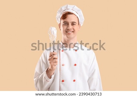 Male confectioner in uniform holding whisk with whipped meringue on beige background