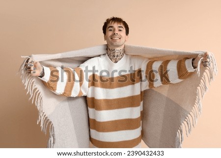 Young man with plaid opening arms for hug on beige background