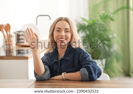 Beautiful young woman waving hand in kitchen at home