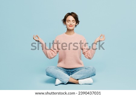 Full body young woman she wear beige knitted sweater casual clothes sit hold spreading hands in yoga om aum gesture relax meditate try to calm down isolated on plain pastel light blue cyan background Royalty-Free Stock Photo #2390437031