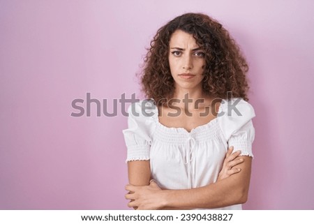 Hispanic woman with curly hair standing over pink background skeptic and nervous, disapproving expression on face with crossed arms. negative person. 