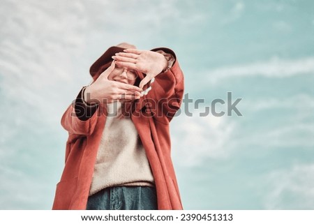 Teenage girl in a red coat and hat stands against the sky and makes a frame shot with her hands. Royalty-Free Stock Photo #2390451313