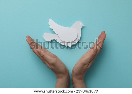 Decorative paper bird and hands on blue background, top view
