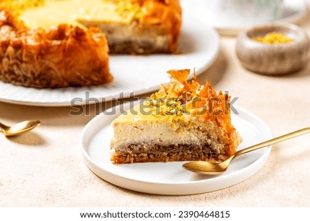 A piece of homemade Baklava cheesecake with pistacchio. Light cream cheese filling on top of walnut-filled filo pastry layers soaked in aromatic honey syrup. Sweet pastry, baked dessert. Royalty-Free Stock Photo #2390464815