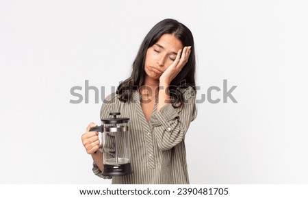 young hispanic woman feeling bored, frustrated and sleepy after a tiresome and holding a manual coffee maker