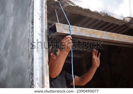 The builder is at work. Indonesia, November 20, 2023, the worker is holding and lifting the iron door, the shop building is being worked on, the iron door so that the shop can be opened wide