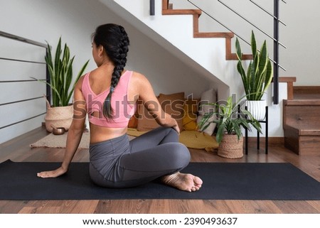 Young woman doing seated twist yoga pose at home. Active and healthy lifestyle. Royalty-Free Stock Photo #2390493637