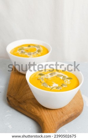 Two white bowls of pumpkin cream soup with dried seeds and thyme leaves on a wooden cutting board on a gray background. Concept of healthy eating. Vegetarian and vegan food. Vertical orientation.