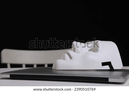 Mask and laptop on white table against black background, closeup Royalty-Free Stock Photo #2390510769