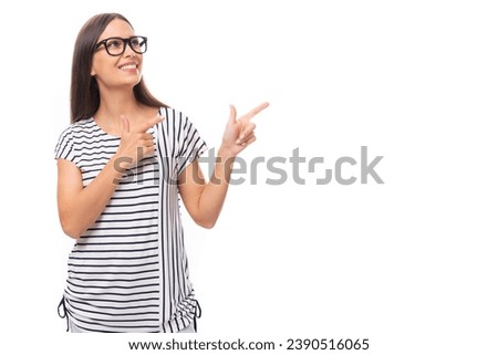 young beautiful brunette lady with straight hair dressed in a striped t-shirt and jeans points her finger to the side on a white background with copy space