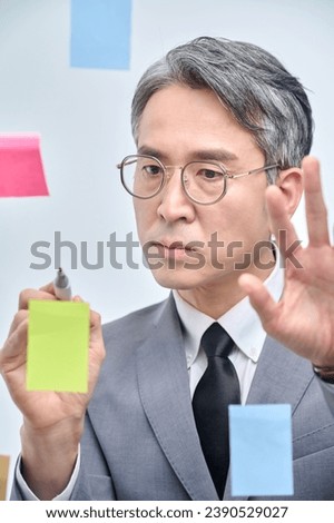 The businessman is standing on the glass wall of the office, looking at the paper attached, thinking about planning and strategies.