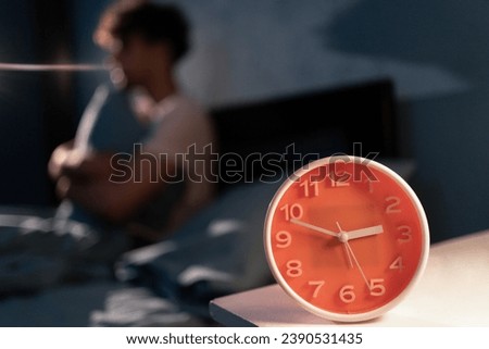 Muslim man in bed suffering insomnia at night and sleep disorder thinking about his problem. Alarm clock in the focus. Copy space Royalty-Free Stock Photo #2390531435