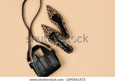 Leopard print shoes and black handbag on beige background. Fashion spring, summer or autumn outfit. Women's stylish and elegant clothes with accessory.  Flat lay, top view, overhead.
