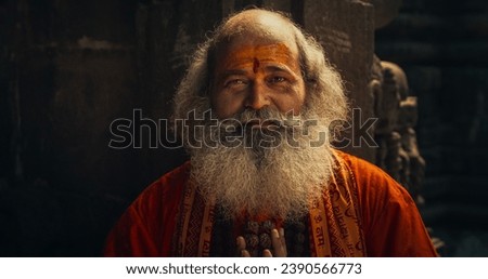 Portrait of a Senior Hindu Monk Looking at the Camera and Smiling While Wearing a scarf Written: "Rattan Mohan Sharma Om Namah Shivay." in an Ancient Temple. Friendly Indian Senior Man Posing  Royalty-Free Stock Photo #2390566773