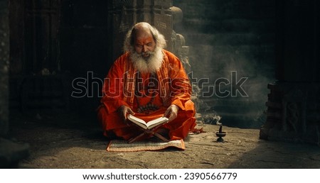Portrait of Old Indian Monk Reading a Book in an Ancient Temple. Senior Guru Getting Wisdom from Sacred Texts, While Wearing a scarf Written: "Rattan Mohan Sharma Om Namah Shivay." Royalty-Free Stock Photo #2390566779