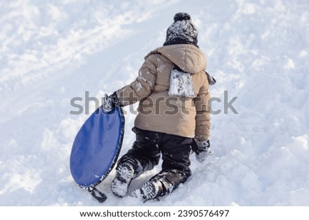 happy boy slides down an ice slide in winter outside Royalty-Free Stock Photo #2390576497