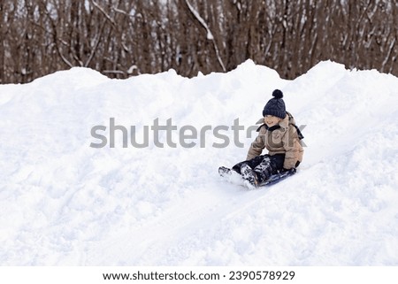 happy boy slides down an ice slide in winter outside Royalty-Free Stock Photo #2390578929