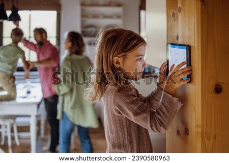 Girl looking at smart thermostat at home, checking heating temperature. Concept of sustainable, efficient, and smart technology in home heating and thermostats. Royalty-Free Stock Photo #2390580963