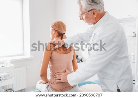 Mature male orthopedist in eyeglasses examining female patient's back in clinic. Spinal injury treatment. Reflexology concept. Healing after trauma in hospital. Vertebrae dislocation