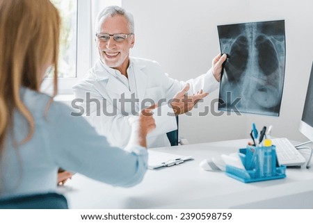 Senior doctor showing xray to his patient in medical office. Pulmonology concept. Coronavirus pneumonia treatment. Cough and flu. Lungs of smoker nonsmoker Royalty-Free Stock Photo #2390598759