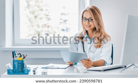 Middle aged female doctor sitting at desk and using digital tablet in office. Telemedicine. General practitioner family doctor gynecologist checking on diagnosis, sending test results online Royalty-Free Stock Photo #2390598781