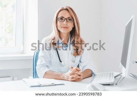 Portrait of adult female doctor sitting at desk in office clinic. Nurse gynecologist therapist general practitioner listening to patient. Telemedicine Royalty-Free Stock Photo #2390598783