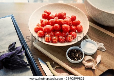 High angle view of plate with tomatoes on cutting board near oven tray with ingredients on wooden background. High quality photo