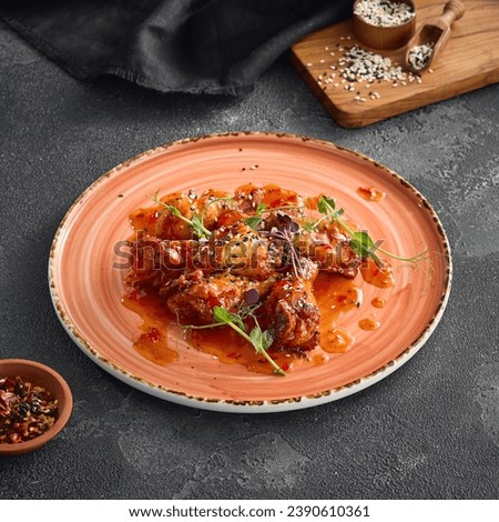 Crispy fried chicken wings doused in a luscious sweet chili sauce, delicately placed on a round ceramic plate, accentuated by a dark background. Royalty-Free Stock Photo #2390610361