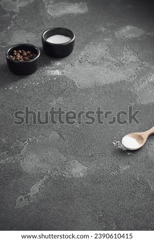Artistic composition of cooking essentials with black bowls of allspice and salt, and a wooden spoon on a dark textured surface, perfect for culinary themes.